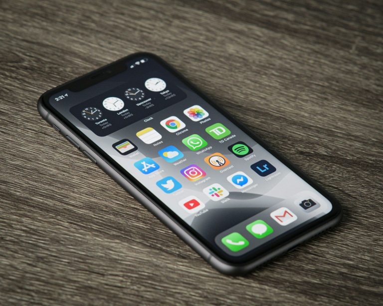 A smartphone with a home screen full of app icons on a wooden surface